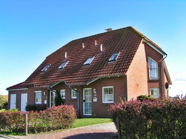 Een twee verdiepingen tellend bakstenen huis met schuin dak, een veranda en een kleine tuin.
