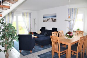 Een woonkamer met een bank, eettafel, stoelen en een trap.