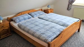 A double bed with a wooden frame, two bedside tables with lamps, and a radiator on the wall. - Flüthörn - Cozy semi-detached house with unobstructed views (Norden)