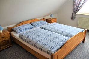 Een tweepersoonsbed met houten frame, twee nachtkastjes met lampen, en een radiator aan de muur.