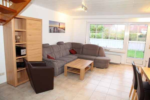 A living room with a sectional sofa, a wooden coffee table, a TV stand, and a large window with a view of greenery.