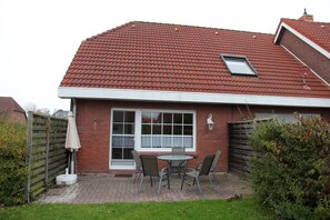 A house with a red tiled roof, a large window with a white frame, and a small skylight. There is a patio with a table and chairs, and a wooden fence in the background.