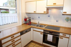 A compact kitchen with white cabinets, a wooden countertop, a built-in dishwasher, and a stove.