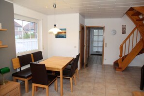A dining area with a wooden table and chairs, a pendant light, and a view of the outside through a window.