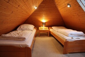 A cozy attic bedroom with two wooden bunk beds, a nightstand, and a lamp.
