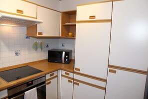 Cozinha compacta com armários brancos, micro-ondas preto e bancada de madeira.