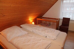 A bedroom with a wooden ceiling, a crib, a chair, and a bedside lamp.