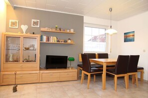 A modern living room with a dining area, featuring a TV, wooden furniture, and a window with a view.