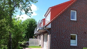 A brick house with a red roof, a small balcony, and a white fence. - Wattwunder - Schöne Ferienwohnung mit Inkludiertem Strandkorb am Strand (Norden)