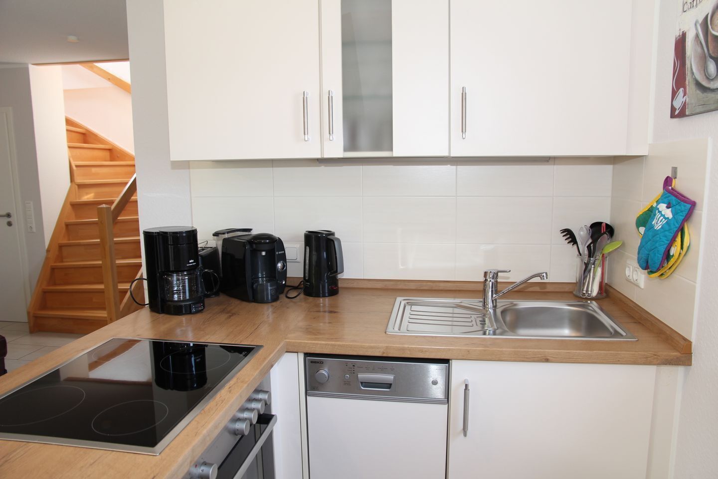 Een kleine keuken met witte kastjes, een spoelbak, een vaatwasser, een fornuis en een koffiezetapparaat.