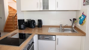 A compact kitchen with white cabinets, a sink, a dishwasher, a stove, and a coffee maker. - Wattwunder - Schöne Ferienwohnung mit Inkludiertem Strandkorb am Strand (Norden)