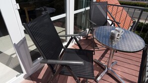 A balcony with a glass door, two chairs, and a small table with a metal top and two mugs. - Wattwunder - Schöne Ferienwohnung mit Inkludiertem Strandkorb am Strand (Norden)