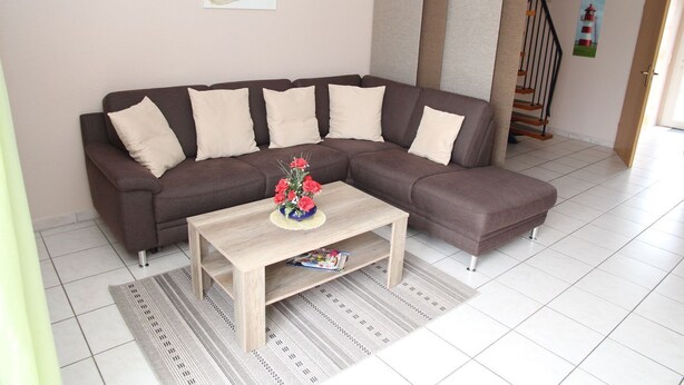A living room with a brown sectional sofa, a wooden coffee table with a vase of red flowers, and a staircase in the background. - Sandrose - Semi-detached house (85sqm) for 4 persons with garden in a direct (Norden)
