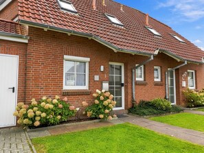 A two-story brick house with a red-tiled roof, a front door, and a small garden with hydrangea bushes. - Sandrose - Semi-detached house (85 m²) for 4 people with a garden right on the beach (Norden)