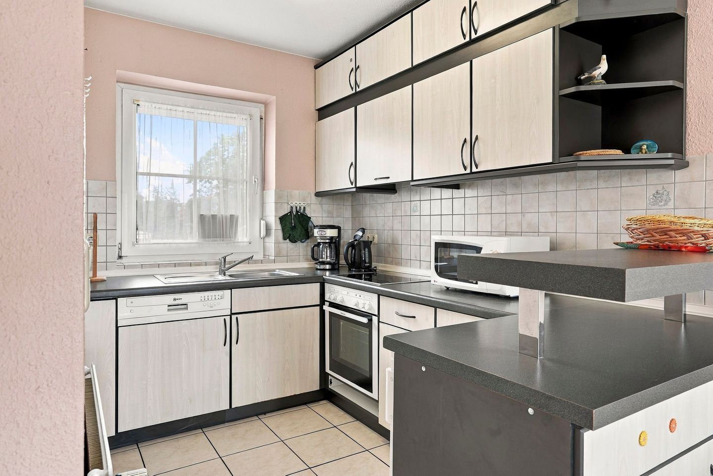 Una cucina moderna con mobili chiari in legno, un piano di lavoro nero, un forno a microonde e una macchina per il caffè.