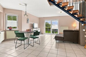 A modern living room with a staircase, a dining area with chairs, and a television. - Sandrose - Semi-detached house (85 m²) for 4 people with a garden right on the beach (Norden)