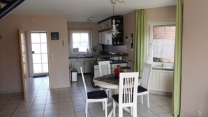A compact kitchen with white cabinets, a dining table with four chairs, and a window with green curtains. - Sandrose - Semi-detached house (85sqm) for 4 persons with garden in a direct (Norden)