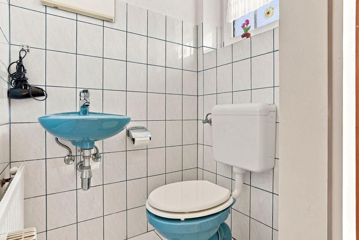 A bathroom with a blue sink, white toilet, and a towel dispenser.