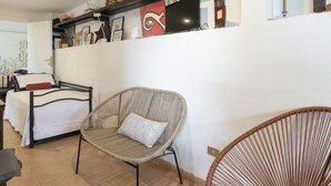 Een kamer met een bed, een rieten stoel, een plank met decoratieve objecten en een aan de muur bevestigde televisie.