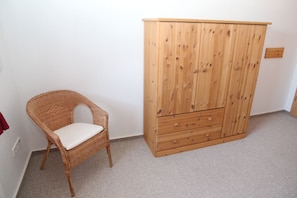 Une pièce avec un fauteuil en osier et une armoire en bois.