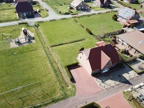 Vue aérienne d’un quartier résidentiel avec des maisons, une aire de jeux et des panneaux solaires sur les toits.