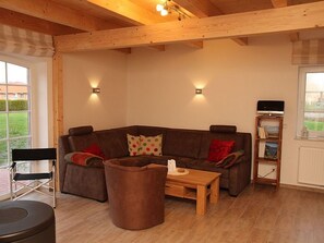 A living room with a brown sectional sofa, a wooden coffee table, a black chair, and a bookshelf with books and a TV. - Aloha - Aloha in Greetsiel: 3 bedrooms, wood-burning stove, garden and WLAN (Krummhörn)