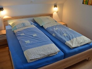 En dubbelsäng med blått sänglinne och en sänggavel i trä. Det finns sänglampor och en vägglampa.