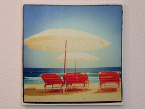 A beach scene with three red lounge chairs and a large white umbrella.