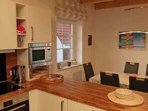 Une cuisine équipée d’un four à micro-ondes, d’un four et d’une machine à café. On y trouve une table à manger avec des chaises, et un chapeau posé dessus.