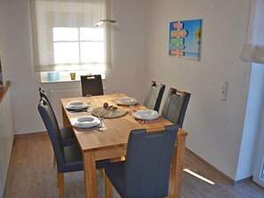 Een eetgedeelte met een houten tafel, vier stoelen en een raam met jaloezieën.