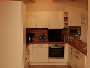 Une cuisine moderne avec des meubles blancs, un four encastré, un four à micro-ondes et une machine à café.