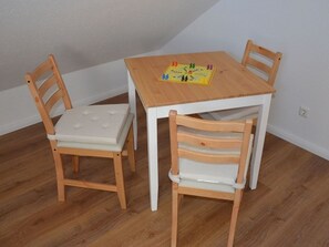 Une petite pièce avec une table en bois et deux chaises, un jeu de société sur la table et un mur blanc.