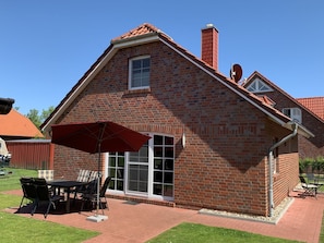 Een bakstenen huis met een terras, een tafel met stoelen en een rode parasol.
