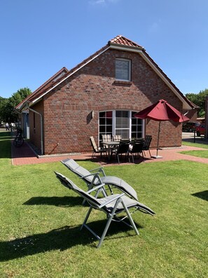 Een stenen huis met terras, buitenmeubels en een rode parasol.