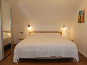 Een eenpersoonsbed met een witte dekbedovertrek in een kamer met houten vloer, een deur en twee wandlampen.