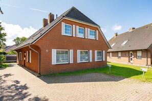 Kaksikerroksinen tiilitalo, jossa on valkoiset ikkunaluukut, päällystetty ajotie ja nurmikko.