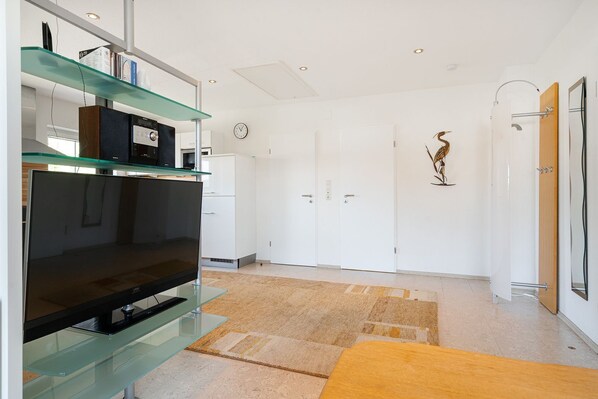 A modern living room with a glass TV stand, white cabinets, a wooden bench, and a decorative plant.