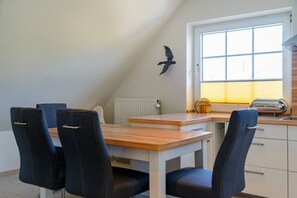 Un coin repas avec une table en bois et quatre chaises, une fenêtre avec des stores et un radiateur.