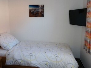 Une chambre à coucher avec un lit, un téléviseur fixé au mur et un tableau.