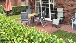 Une maison avec un toit recouvert de tuiles rouges, une façade en briques et un patio abrité aménagé avec du mobilier d’extérieur.