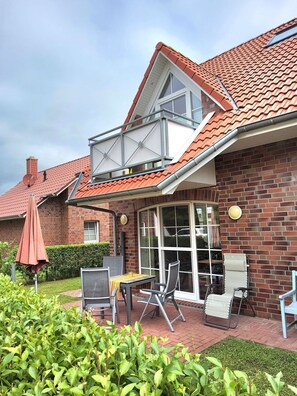 Ein Haus mit rotem Ziegeldach, einer Ziegel-Fassade und einer überdachten Terrasse mit Gartenmöbeln.
