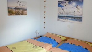 Une chambre avec deux lits, une lampe fixée au mur et deux tableaux représentant des scènes de nature.