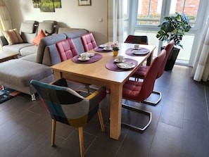 Un coin repas avec une table en bois, des chaises à revêtement rouge et un canapé gris.