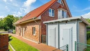 Une maison à deux étages avec un toit recouvert de tuiles rouges, une façade en briques et un petit garage attenant avec des portes blanches.