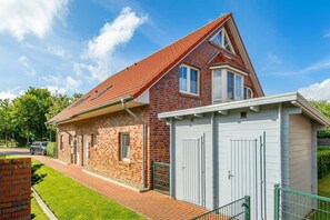 Ein zweistöckiges Haus mit rotem Ziegeldach, einer Ziegel-Fassade und einer kleinen angebauten Garage mit weißen Türen.