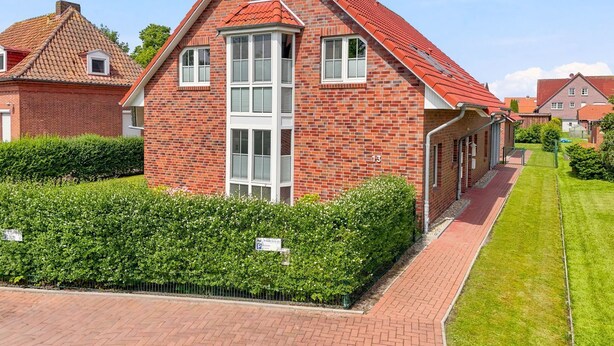 Une maison en briques rouges, avec un toit à pignon, une cheminée centrale et une pelouse bien entretenue.
