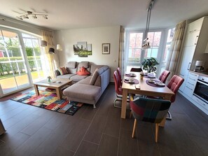 Una sala moderna con un sofá, una mesa de comedor para cuatro personas y una cocina con armarios y estufa.