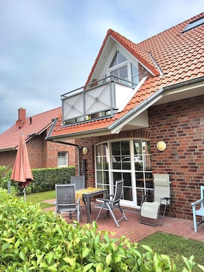 Une maison avec un toit recouvert de tuiles rouges, une façade en briques et un patio abrité aménagé avec du mobilier d’extérieur.