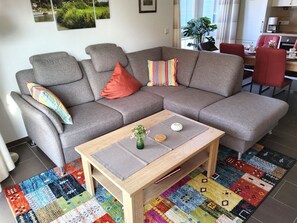 Una sala moderna con un sofá seccional gris, una mesa de centro de madera y una alfombra colorida.