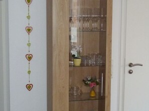 Un meuble en bois doté de portes en verre, contenant divers objets en verre et un vase avec des fleurs.